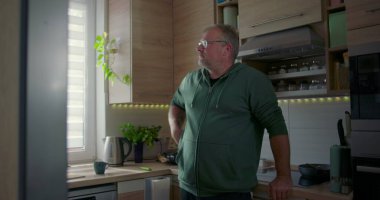 Pencerenin yanında duran adam, düşünceli poz, rahat ev hayatı, ev hayatı, modern mutfak arka planı yeşillik ve doğal ışık