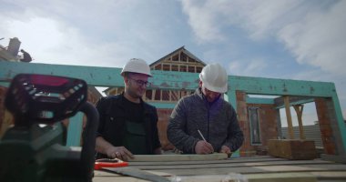 İnşaat sahasında ahşabı, takım çalışmasını işaretleyen ve detaylara, konut projesine, inşaat halindeki eve, çalışma maskesine, aletlere ve malzemelere odaklanan inşaatçılar