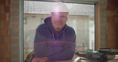 İnşaat işçisi inşaat halindeki tezgahta güvenle gülümsüyor, inşaat alanında güvenlik kaskı takıyor, rahat ve profesyonel atmosfer takıyor.