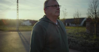 Karanlık çöktüğünde kırsal yolda duran bir adam, sakin bir ifadeyle, arka planda gün batımı parıltısı, kırsal bir manzara, huzurlu bir an, açık bir manzara, kırsal alanda yalnızlık.