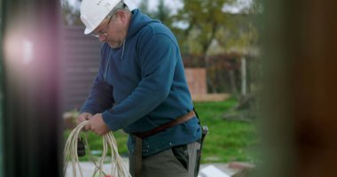 İnşaat sahasında miğferi olan işçilere kablo taşıyıp düzenlemek, el işçiliği ve dışarıda profesyonel aktiviteler sergilemek.