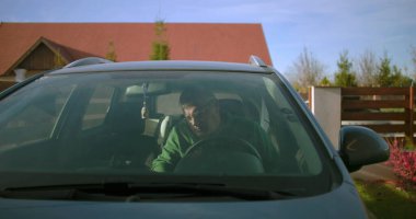 Bir adam konut yolunda sürücü tarafından arabaya biniyor, sürmeye hazırlanıyor, bir yolculuğa ya da her gün işe gidip gelmeye odaklanıyor