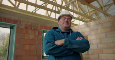 Kollarını kavuşturmuş, kasketli, kısmen inşa edilmiş bir binada duran kendine güvenen bir inşaat işçisi. İşinde profesyonelliği ve gururu somutlaştırıyor.