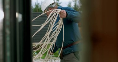 İnşaat sahasında miğferi olan işçilere kablo taşıyıp düzenlemek, el işçiliği ve dışarıda profesyonel aktiviteler sergilemek.