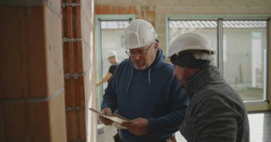 İnşaat işçisi tuğla duvarı ve mühendis gözlemi, inşaat sahasında açık duvarları ve geniş pencereleri olan takım çalışması