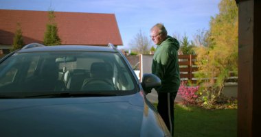 Bir adam konut yolunda sürücü tarafından arabaya biniyor, sürmeye hazırlanıyor, bir yolculuğa ya da her gün işe gidip gelmeye odaklanıyor