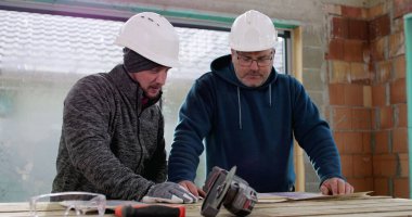 İnşaat ekibi inşaat başlıkları ve aletleri ile bir binanın içinde tadilat, takım çalışması, plan analizi ve çalışma planlarını tartışıyor.