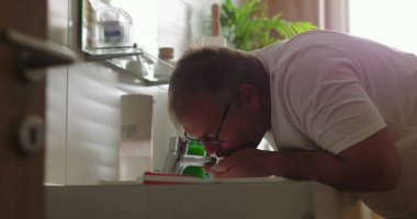 Banyodaki lavabodan gelen suyla ağzını çalkalayan adam, parlak ve temiz minimalist ortamda ağız hijyenine ve özgüvenine odaklanıyor.