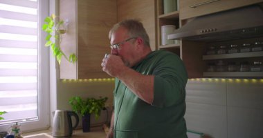 Mutfakta bardaktan içen bir adam, sabah rutini, sıcak bir içecek, sıradan bir ev hayatı, doğal ışık ve yeşillik ile modern mutfak.