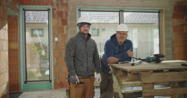 İnşaat alanındaki inşaat, takım çalışması ve güvenlik, işçilik ve adanmışlık alanlarındaki alet ve atölyenin yanında güven içinde poz veren inşaat işçileri