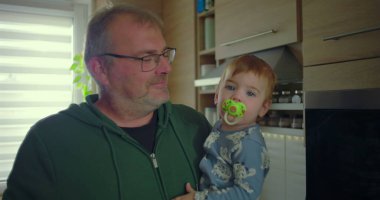 Baba, bebeğini emzik ile tutarken gülümsüyor, sıcak ve samimi anın tadını çıkarıyor.