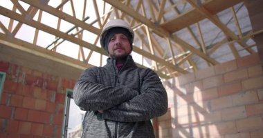 İnşaat işçisi, henüz tamamlanmamış bir binanın içinde güvenle duruyor. Kararlılığı, takım çalışmasını ve inşaat uzmanlığını temsil ediyor.