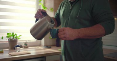 Sıcak suyu fincana, mutfak aktivitesine, sabah rutinine, çay ya da kahve yapımına, ev hayatı tarzına, doğal ışık ile modern iç mekanlara döken ellerin yakın çekimi