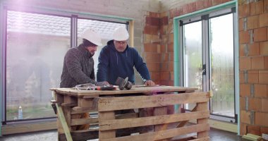 İnşaat ekibi inşaat başlıkları ve aletleri ile bir binanın içinde tadilat, takım çalışması, plan analizi ve çalışma planlarını tartışıyor.