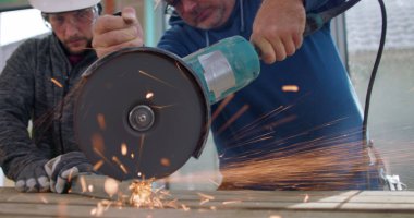 Açı öğütücü kullanan inşaat işçilerinin yakın çekimi, yoğun odaklanma, kıvılcımlar uçuşuyor, metal kesme, yenileme alanında güvenlik teçhizatı ile takım çalışması