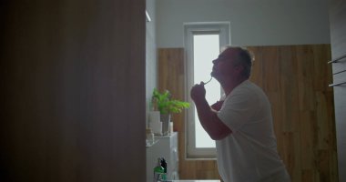 Adam güne hazırlanıyor, jiletle çene ve boyun bölgesini tıraş ediyor, tıraş köpüğünü görünür hale getiriyor, banyo arka planı, doğal detaylar günlük tımarlamaya sıcaklık katıyor.