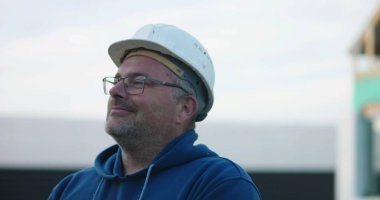 İnşaat işçisi, kasketli, gevşek bir tavırla gülümseyen, inşaat projesinde çalışan, açık havada duran, HOPEFUL ifadesiyle bakan