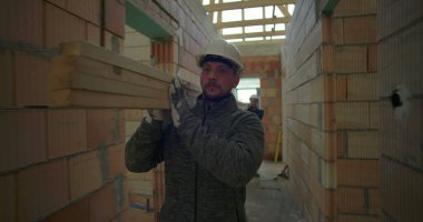 İnşaat işçisi inşaat halindeki evin koridorlarında kalaslar taşıyor ve devam eden inşaat projesinde odak ve güç gösteriyor.