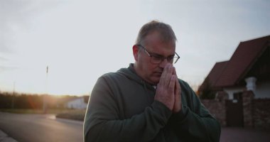 Dışarıdaki adam kollarını havaya kaldırmış, yukarıya bakıyor, minnettarlığını ve umudunu ifade ediyor, kırsal alanda ruhani bir an, sakin ve sakin, günbatımı atmosferi.