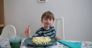 Yemek masasında oturup makarna yemekten zevk alan, çatal tutan, gülümseyen, rahat ve mutlu, sıcak ev ortamında samimi bir aile yemeği zamanı.