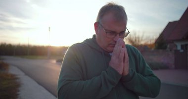 Dışarıdaki adam kollarını havaya kaldırmış, yukarıya bakıyor, minnettarlığını ve umudunu ifade ediyor, kırsal alanda ruhani bir an, sakin ve sakin, günbatımı atmosferi.