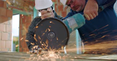 Açı öğütücü kullanan inşaat işçilerinin yakın çekimi, yoğun odaklanma, kıvılcımlar uçuşuyor, metal kesme, yenileme alanında güvenlik teçhizatı ile takım çalışması