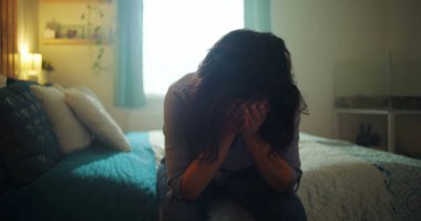 Yatakta oturan bir kadın, başını eğmiş, ellerini yüzünü kapatmış, umutsuzluk, keder ve kayıp, içsel ve derin bir duygusal an tarafından ezilmiş.