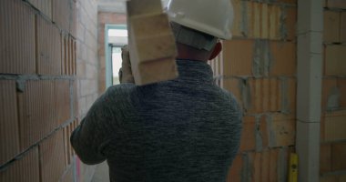 İnşaat işçisi inşaat halindeki konut binasında geniş ahşap kalasları taşırken, işçilere odaklanma ve inşaat ortamında çaba sarfediyor.