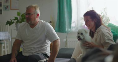 Babam annemi kanepeye oturmuş, kucağında küçük beyaz bir köpek, rahat ev ortamında sıcak bir aile bağı, samimi bir birliktelik anı ve bağ kurarken görüyor.