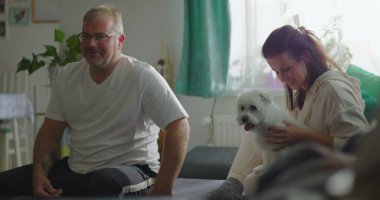 Babam annemi kanepeye oturmuş, kucağında küçük beyaz bir köpek, rahat ev ortamında sıcak bir aile bağı, samimi bir birliktelik anı ve bağ kurarken görüyor.