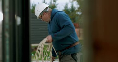İnşaat sahasında miğferi olan işçilere kablo taşıyıp düzenlemek, el işçiliği ve dışarıda profesyonel aktiviteler sergilemek.