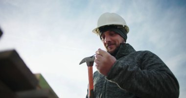 İnşaat işçisi çiviyi çekice çakıyor, tahtaya çakmaya hazırlanıyor, odaklanmış ve inşaat alanında marangozluğa hazır, konut inşaatında hassas ahşap işçiliği.