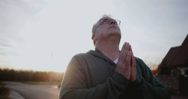 Dışarıdaki adam kollarını havaya kaldırmış, yukarıya bakıyor, minnettarlığını ve umudunu ifade ediyor, kırsal alanda ruhani bir an, sakin ve sakin, günbatımı atmosferi.