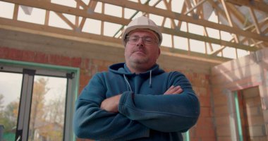 Kollarını kavuşturmuş, kasketli, kısmen inşa edilmiş bir binada duran kendine güvenen bir inşaat işçisi. İşinde profesyonelliği ve gururu somutlaştırıyor.