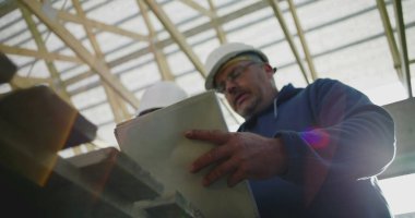 İnşaat denetçisi inşaat planlarını gözden geçirirken aynı zamanda inşaat çalışanı, takım çalışması ve yapısal proje rehberliği, güvenlik kaskları takılı