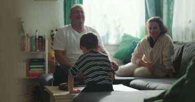 Çocuk kahve masasında oyuncak trenle oynarken ebeveynler rahat bir oturma odasında kanepeden gülümserken, aile zamanının tadını çıkarırken, sıcak ve eğlenceli bir atmosferde.