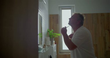 Adam güne hazırlanıyor, jiletle çene ve boyun bölgesini tıraş ediyor, tıraş köpüğünü görünür hale getiriyor, banyo arka planı, doğal detaylar günlük tımarlamaya sıcaklık katıyor.