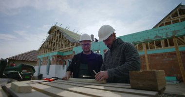 İnşaat sahasında ahşabı, takım çalışmasını işaretleyen ve detaylara, konut projesine, inşaat halindeki eve, çalışma maskesine, aletlere ve malzemelere odaklanan inşaatçılar