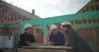 İnşaat işçileri inşaat alanında günlük etkileşim ve dostça sohbetlerin keyfini çıkarıyorlar, başlık takıyorlar, inşaat alanındaki dostluk ve takım çalışmalarını gösteriyorlar.