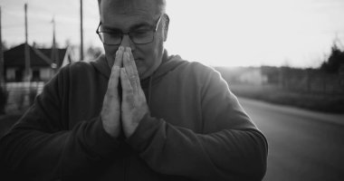 Elleri duada sıkışmış, başı eğik, derin düşüncelere dalmış, huzurlu kırsal alan, siyah beyaz, ruhani an, yansıma ve minnettarlık dolu bir adam.