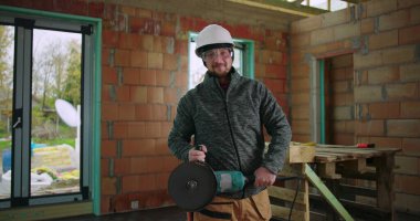 İnşaat işçisi, bina içi, güvenlik teçhizatı, miğfer ve gözlük, inşaat aletleri, sanayi bölgesi gibi görevlere odaklanmış, tamamlanmamış iç mimariye güvenle el değirmeni tutuyor.