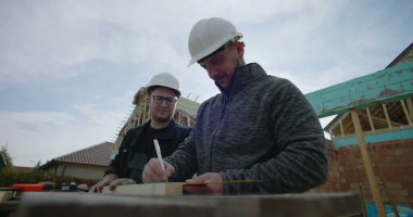 İnşaat alanındaki odunları ölçen müteahhitler, işbirliği çabası, hassas ölçümler, ev iskeleti, takım çalışması, konut projesi, başlıklar, görünür araçlar