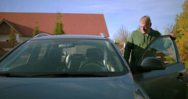 Bir adam konut yolunda sürücü tarafından arabaya biniyor, sürmeye hazırlanıyor, bir yolculuğa ya da her gün işe gidip gelmeye odaklanıyor