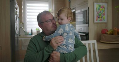 Bebeği mutfakta tutan adam, baba ve bebek arasındaki yakın etkileşim, pijamalı bebek, sıcak aile anı, modern aletlerle mutfak geçmişi.