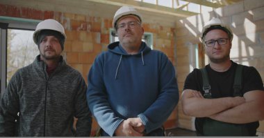 İnşaat ortamında takım çalışması, birlik ve profesyonelliği temsil eden üç inşaat işçisi kısmen inşa edilmiş bir yapıda birlikte duruyorlar.