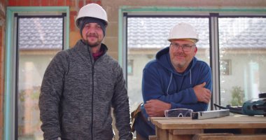 İnşaat işçileri inşaat halindeki çalışma tezgahının yanında gülümsüyor, miğferler takılı, takım çalışması ve inşaat sahasında dostluk, pozitif işyeri atmosferi