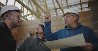 İnşaat ekibi, bitmemiş bir binanın içindeki planları gözden geçirir, inşaat projesinin tasarımını koordine eder ve mimari ayrıntıları tartışır.