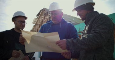 İnşaat işçileri inşaat alanındaki planları gözden geçiriyorlar, inşaat planlamasında takım çalışması, projeyi tartışan sektör profesyonelleri, inşaat geliştirmede işbirliği