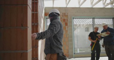Duvarı kalemle ölçen inşaat işçisi, güvenlik miğferinde odaklanmış miğferle içeride tuğla yapı, hassasiyet ve detaylara dikkat ediyor.