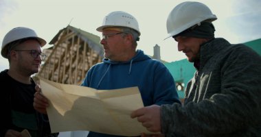 İnşaat işçileri inşaat alanındaki planları gözden geçiriyorlar, inşaat planlamasında takım çalışması, projeyi tartışan sektör profesyonelleri, inşaat geliştirmede işbirliği